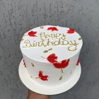 Bolo branco com flores vermelhas pintadas à mão e escrita 'Happy Birthday' em dourado